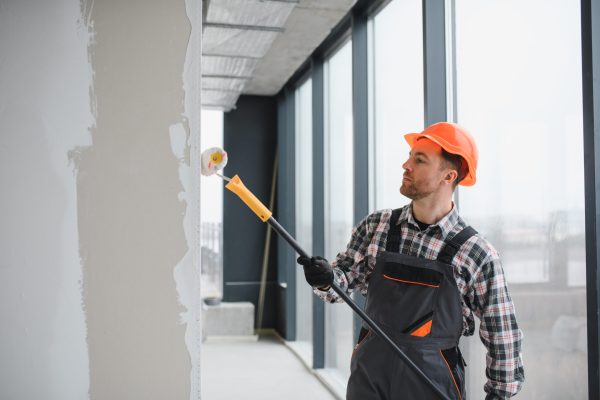 Professional builder using a paint roller, applying a fresh coat of paint to the walls of a building under renovation, demonstrating the process of interior finishing