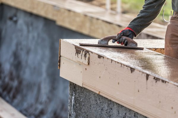 Construction Worker Using Wood Trowel On Wet Cement Forming Coping Around New Pool.