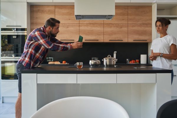 Angry bearded male showing mobile phone to her girlfriend while they standing in the kitchen