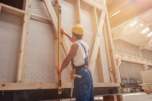 Back view of young man construction worker taking measurements while working on house building project